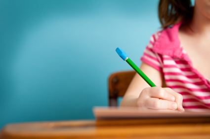 The image shows a child's hand holding a pencil and writing in a book.